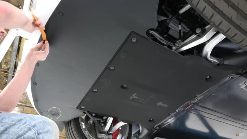 Underside of a Tesla Model 3 showing a speaker grill visible at the front near the bumper.