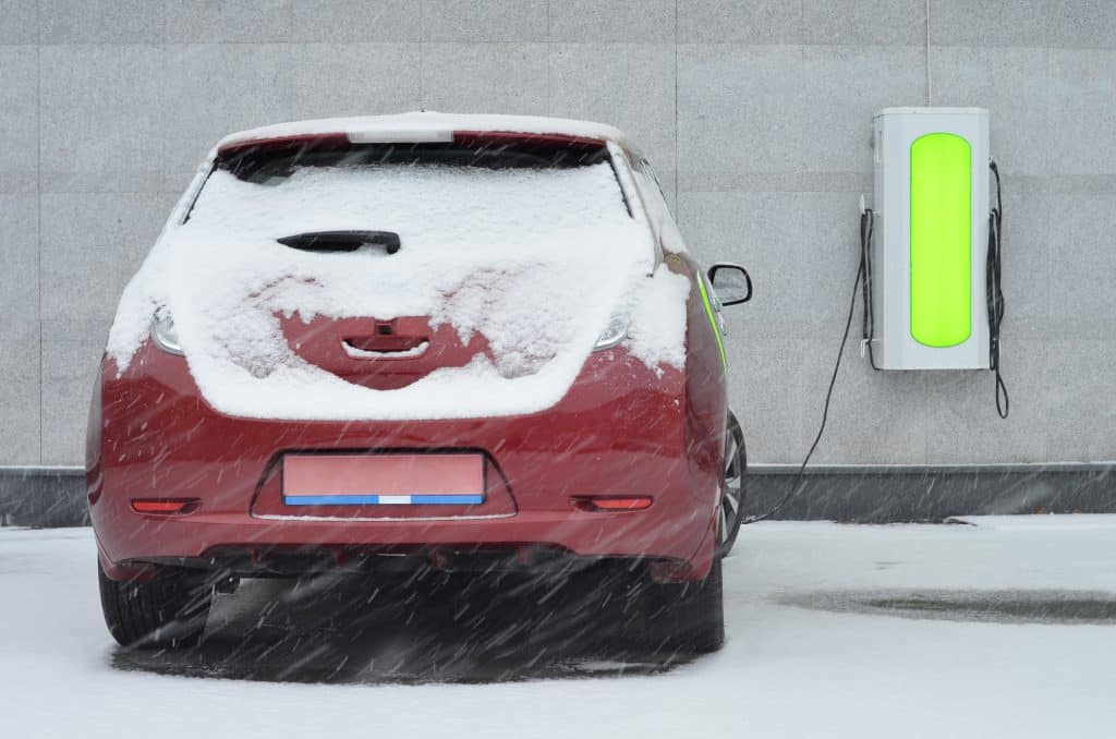 An electric car plugged into a EVSE charging station during snow fall