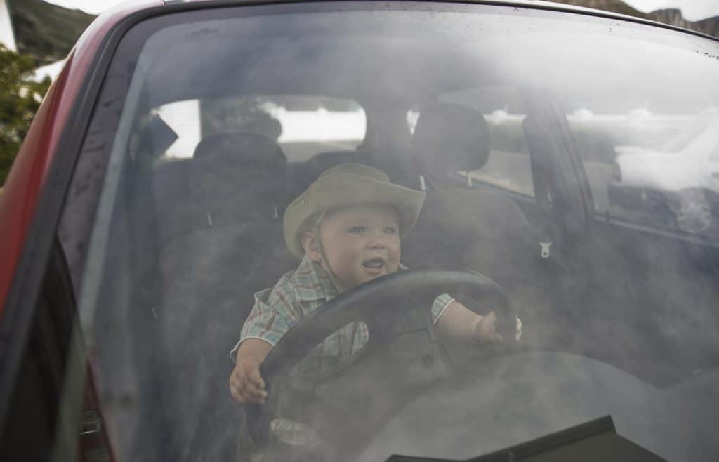 A toddler driving a car wearing a cowbow hat